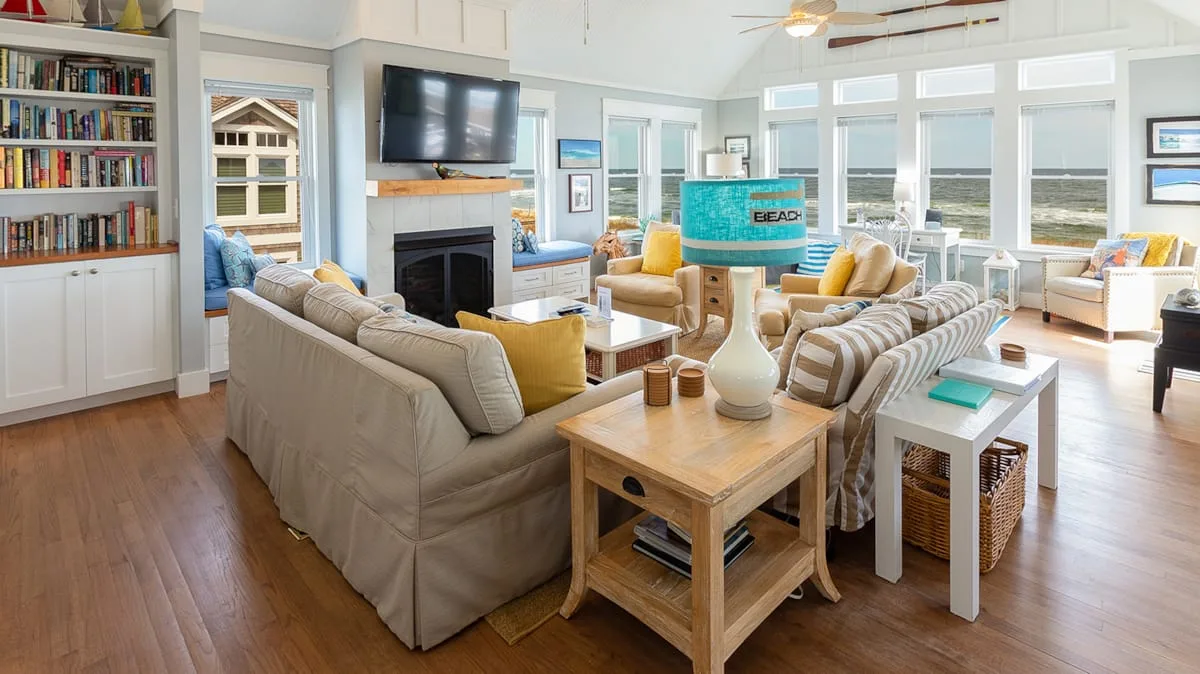 A bright living room with seating arranged around a fireplace and large ocean-facing windows.