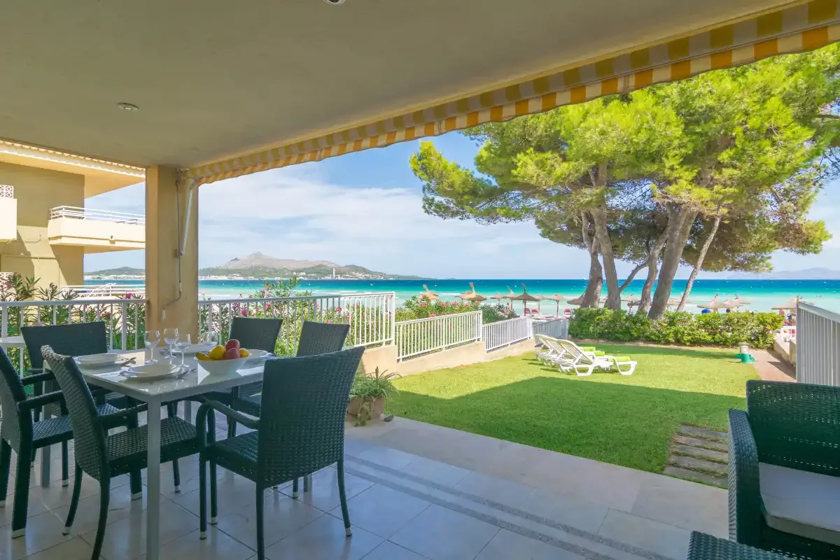 Una zona cubierta para comer al aire libre da a un césped, árboles y el mar.