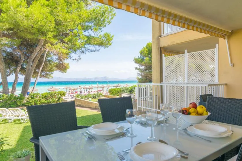 Una zona de comedor al aire libre con sombra da a un césped, pinos y el mar.