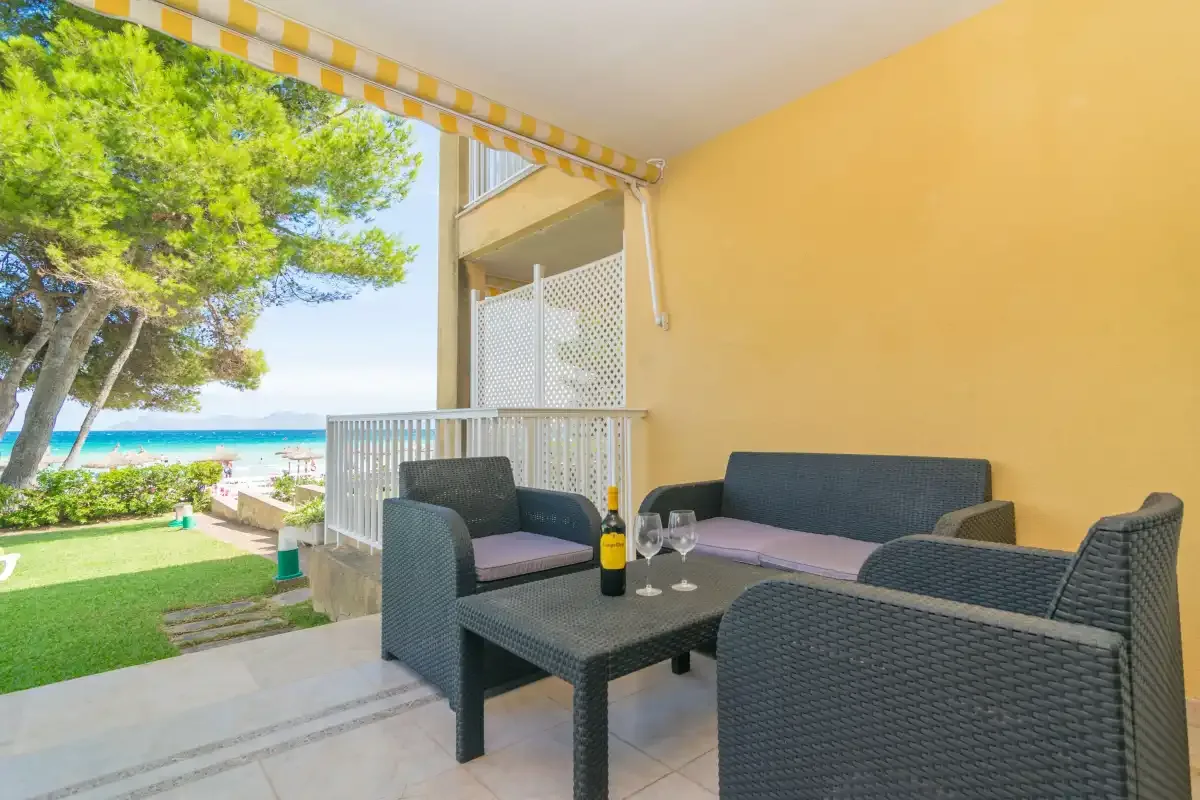 Un patio cubierto con asientos de tejido oscuro da a una zona ajardinada y al mar.