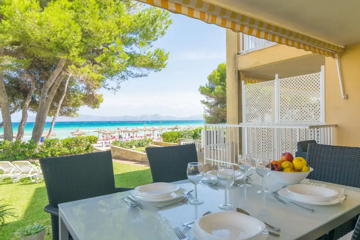 Una zona de comedor en una terraza cubierta da a un césped, árboles y el mar.