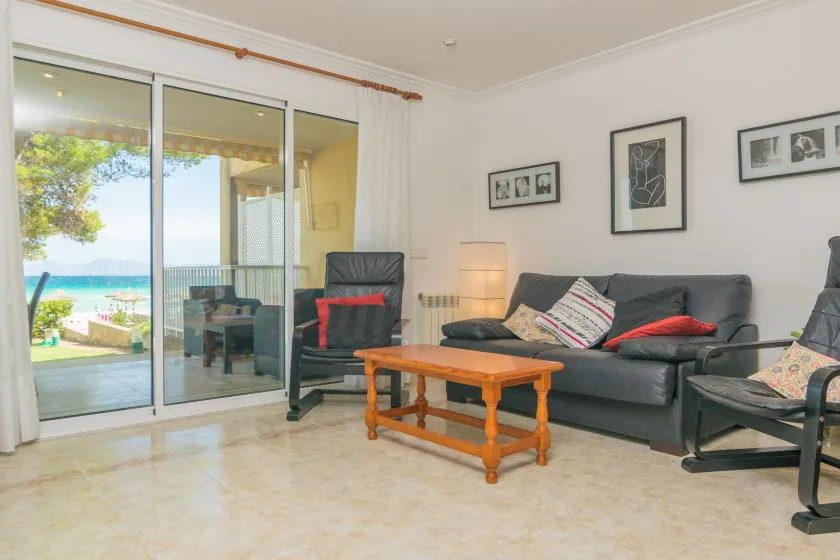 Una sala luminosa tiene asientos, una mesa de centro de madera y puertas corredizas de vidrio.