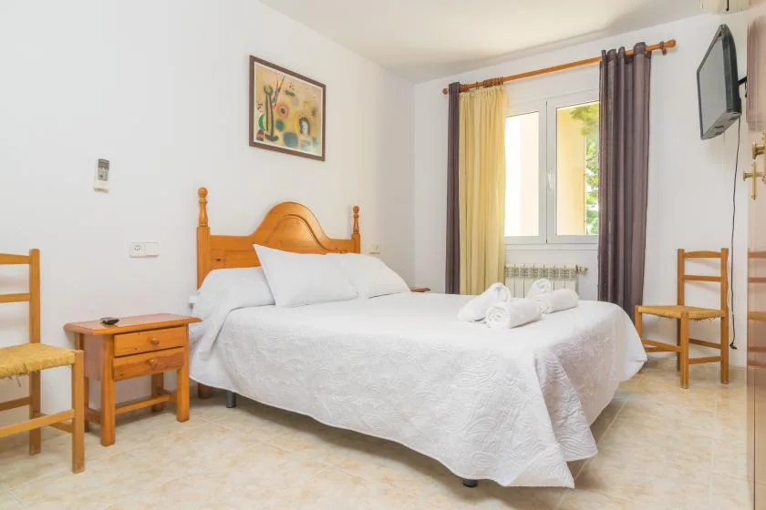 Un dormitorio luminoso con una cama tendida junto a una ventana.