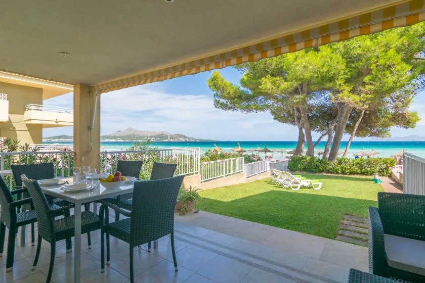 Comedor en una terraza cubierta con vistas al césped, los árboles y el mar.