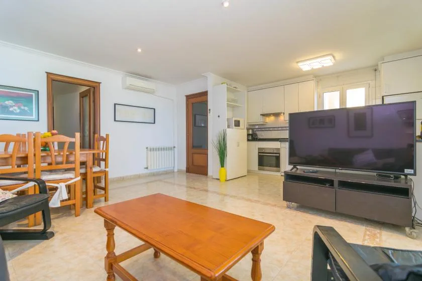 Una sala de estar y comedor con televisor, mesa de comedor y cocina al fondo.