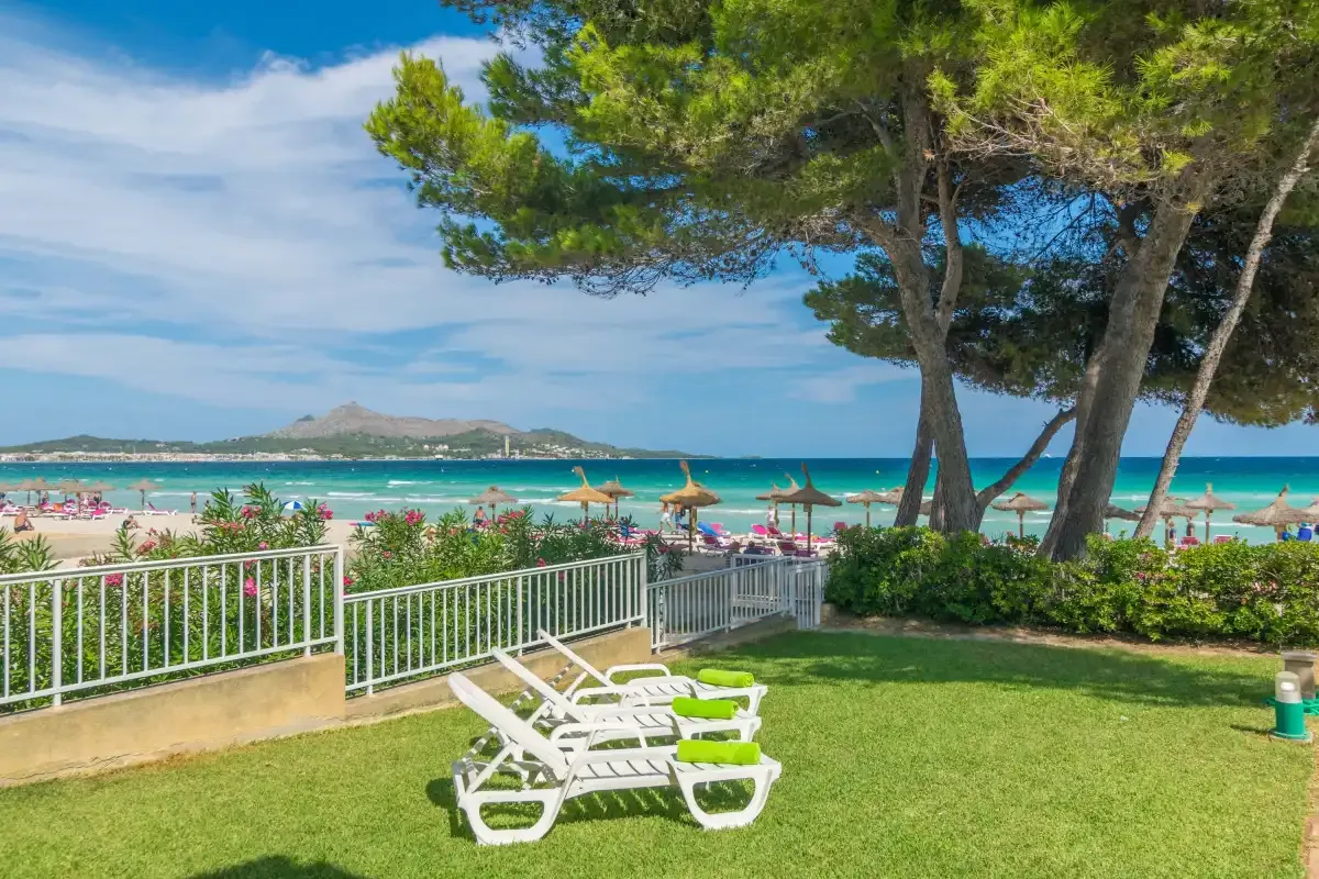 Un jardín frente a la playa, con césped y tumbonas, da al mar turquesa.