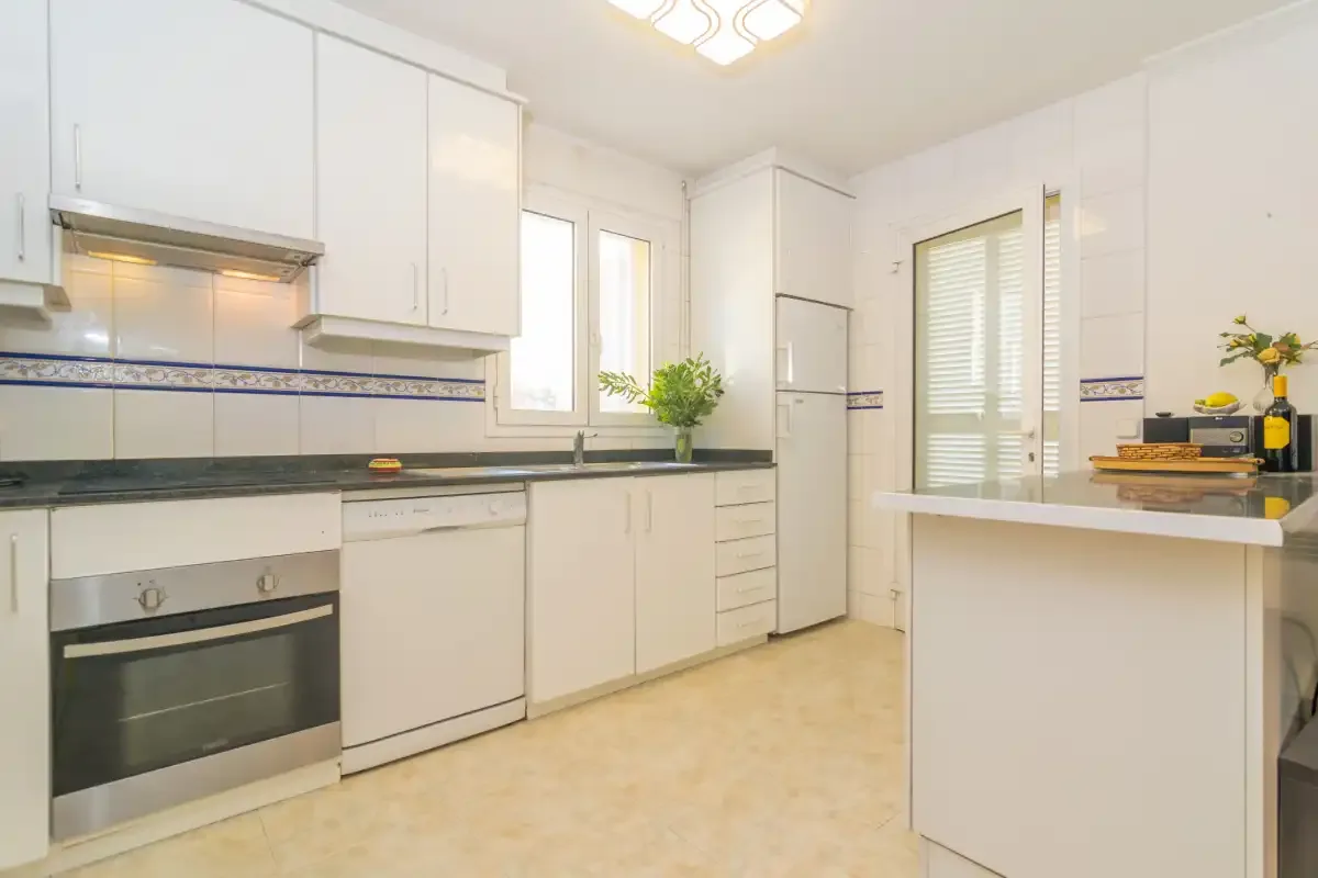 Una cocina blanca y luminosa con encimeras y electrodomésticos integrados.