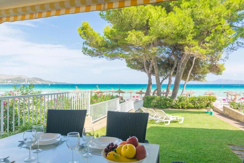 A seaside patio dining area overlooks a grassy lawn, trees, and the beach.