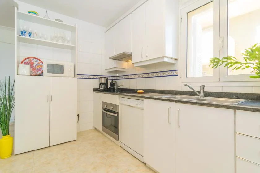 Una cocina luminosa con armarios blancos, una encimera y una ventana.