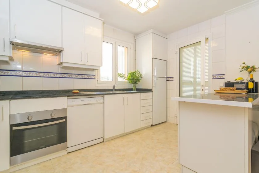 Una cocina luminosa con gabinetes blancos, horno y una encimera central.