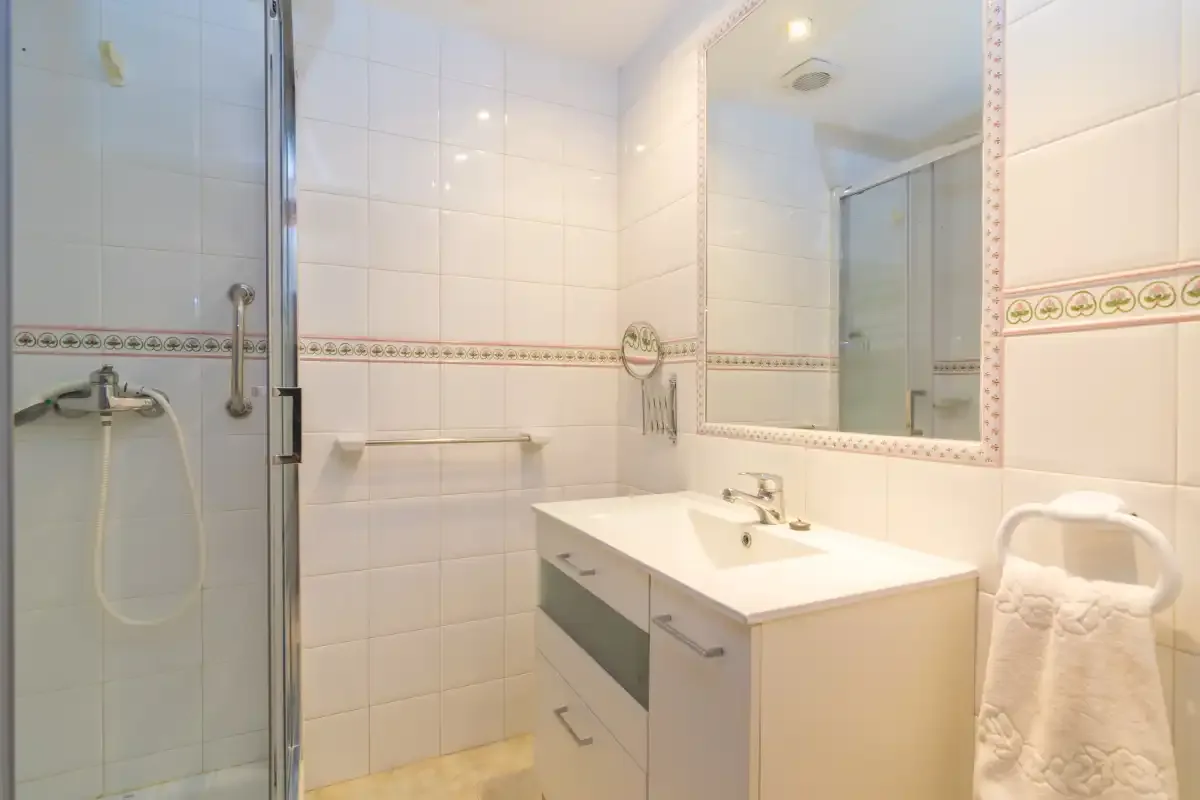 Un baño alicatado con ducha de vidrio, lavabo y un espejo grande.