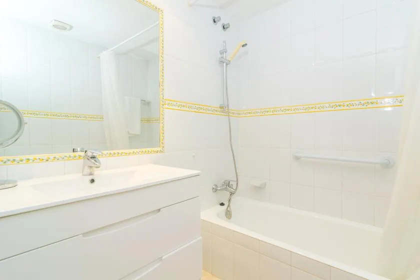 Un baño luminoso con azulejos, bañera, ducha y lavabo con mueble.