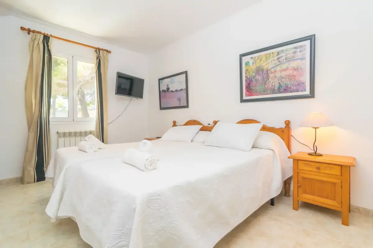 Un dormitorio luminoso con una cama grande, una mesita de noche y cuadros enmarcados.