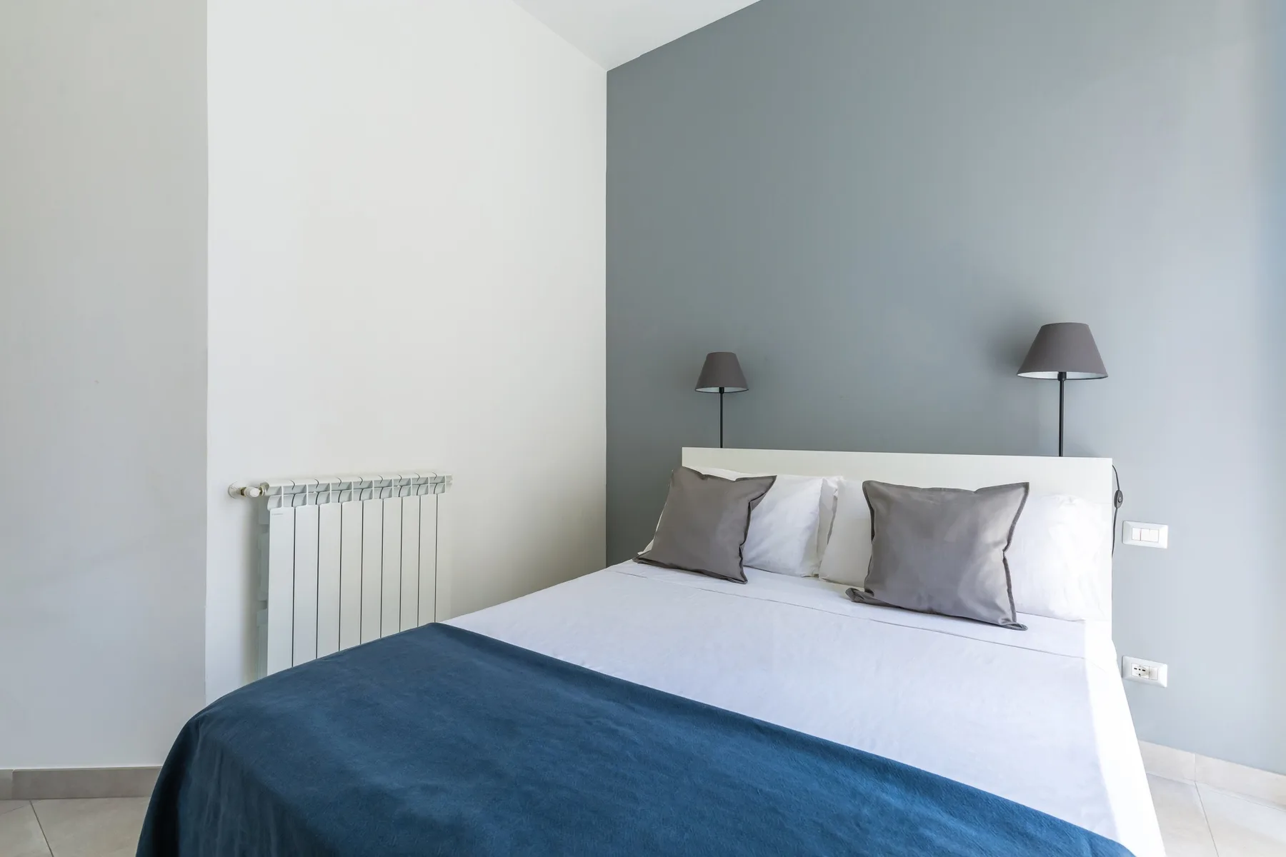 A bedroom with a bed dressed in white linens and a dark blue blanket.