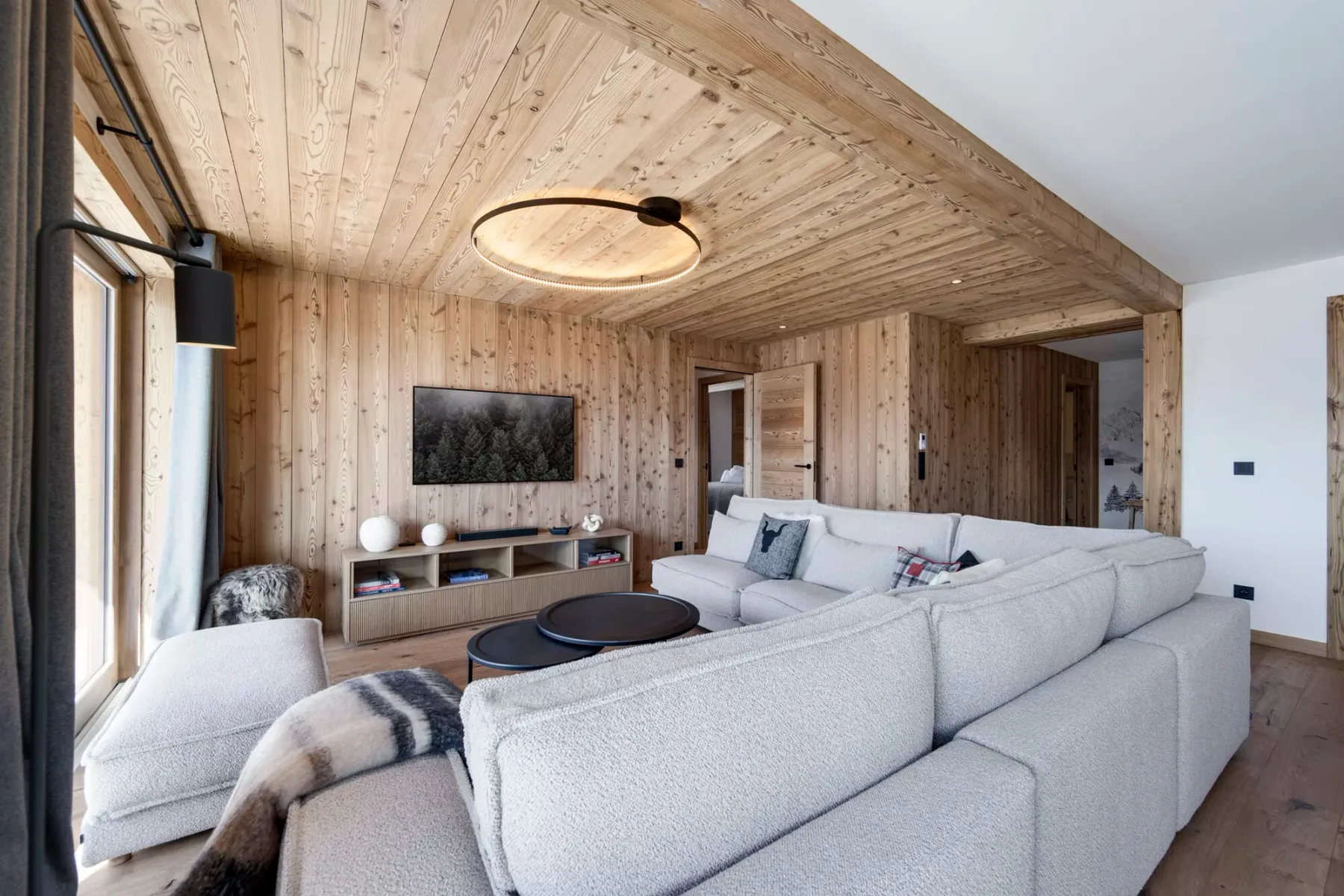 A bright living room with light wood walls and gray seating around a television.