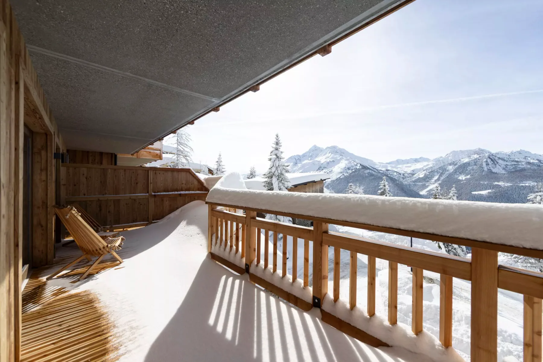 Un balcón cubierto de nieve con barandillas de madera da a un paisaje montañoso.