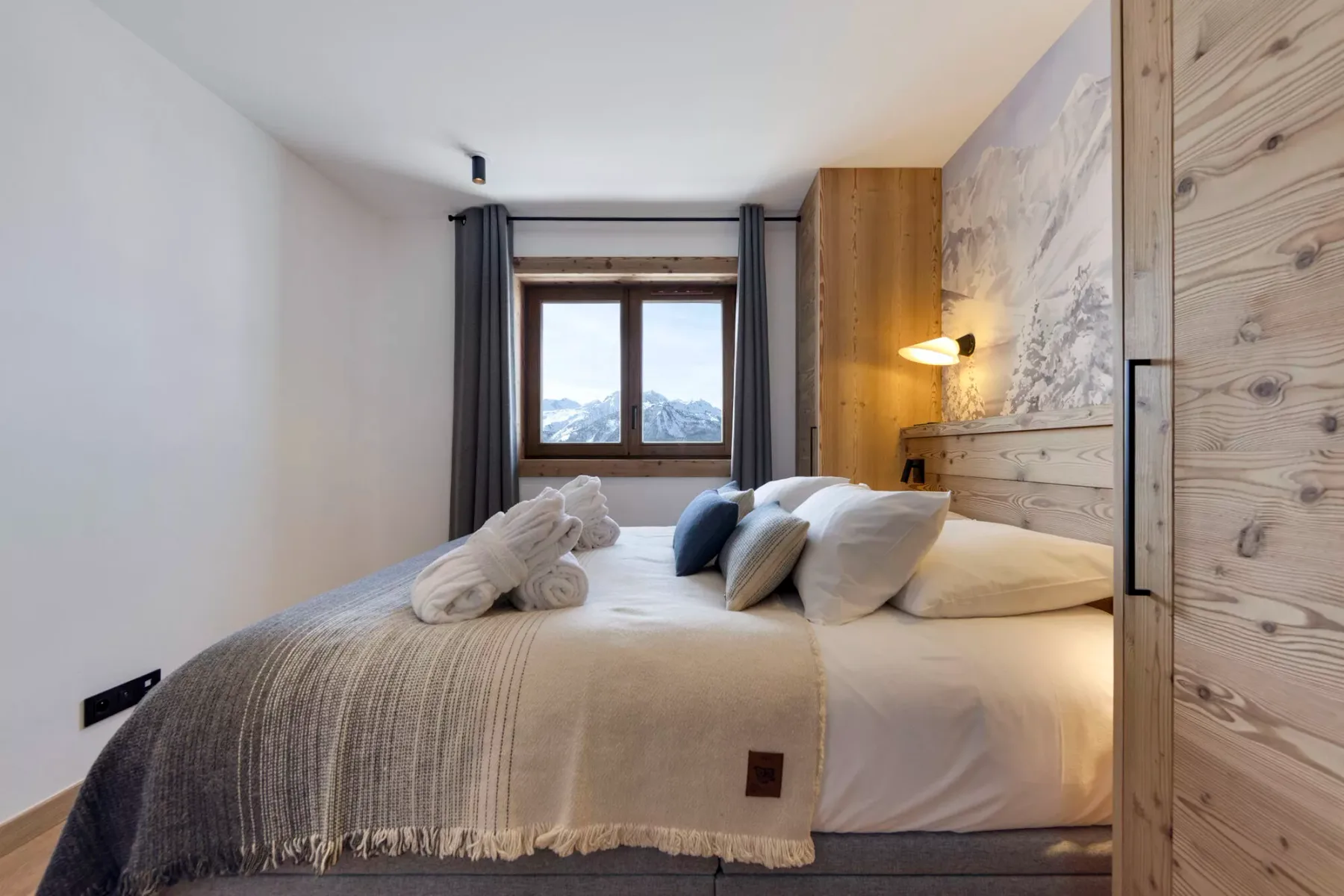 Un dormitorio con una cama bien hecha y una ventana con vistas a las montañas.