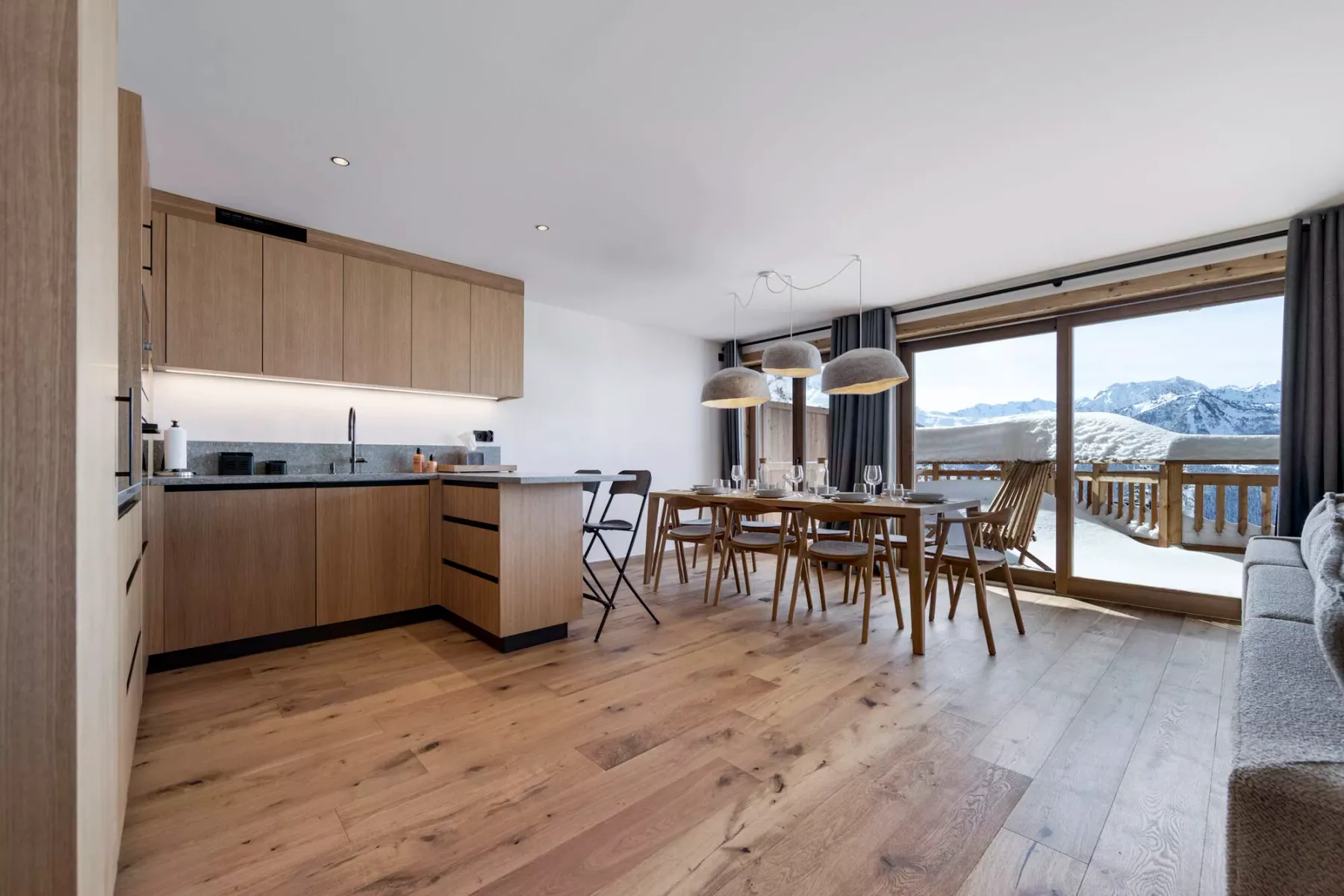 Una cocina abierta con comedor da a un balcón y montañas nevadas.