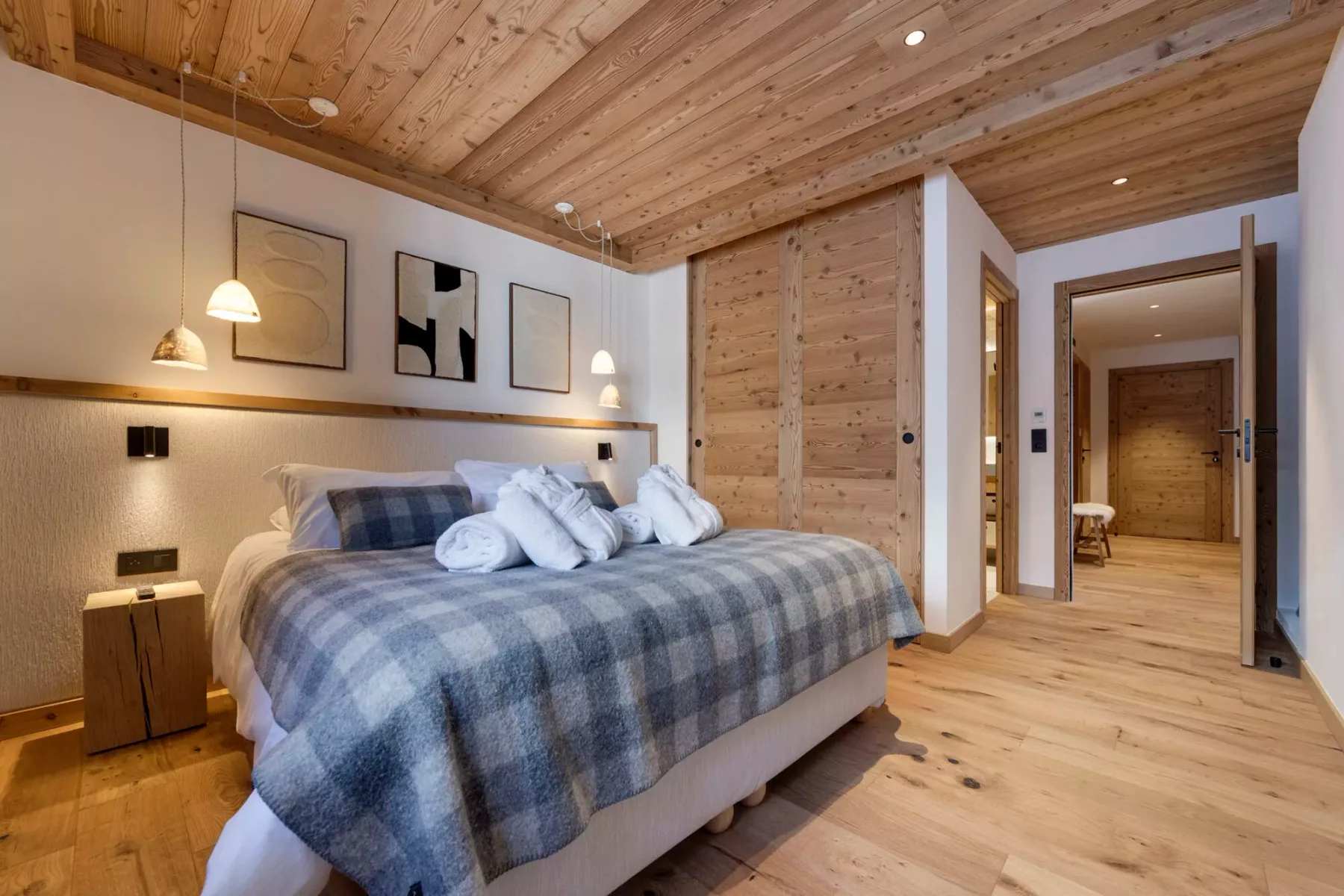 Dormitorio con una cama cubierta por una manta de cuadros grises y techo revestido de madera.