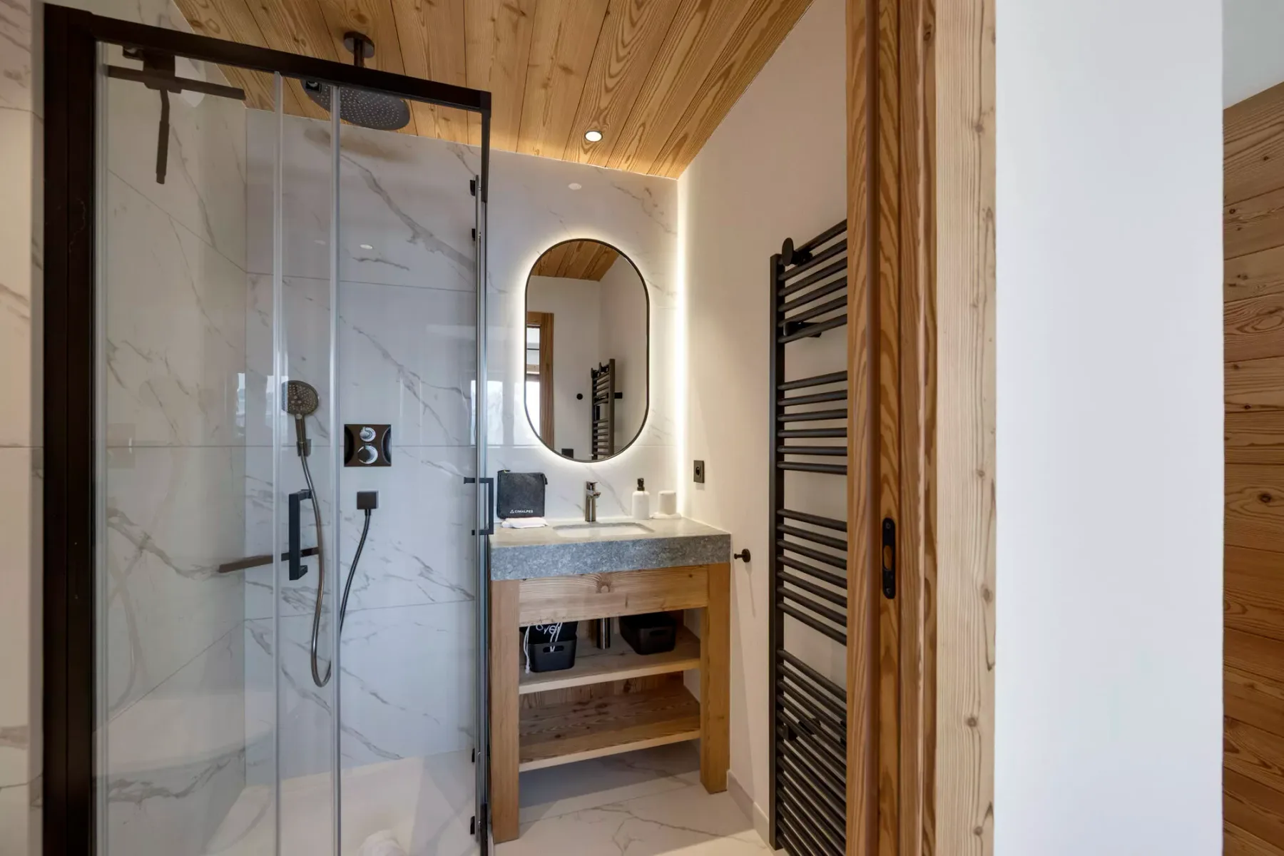 Un baño con ducha de vidrio, tocador y calentador de toallas en la pared.