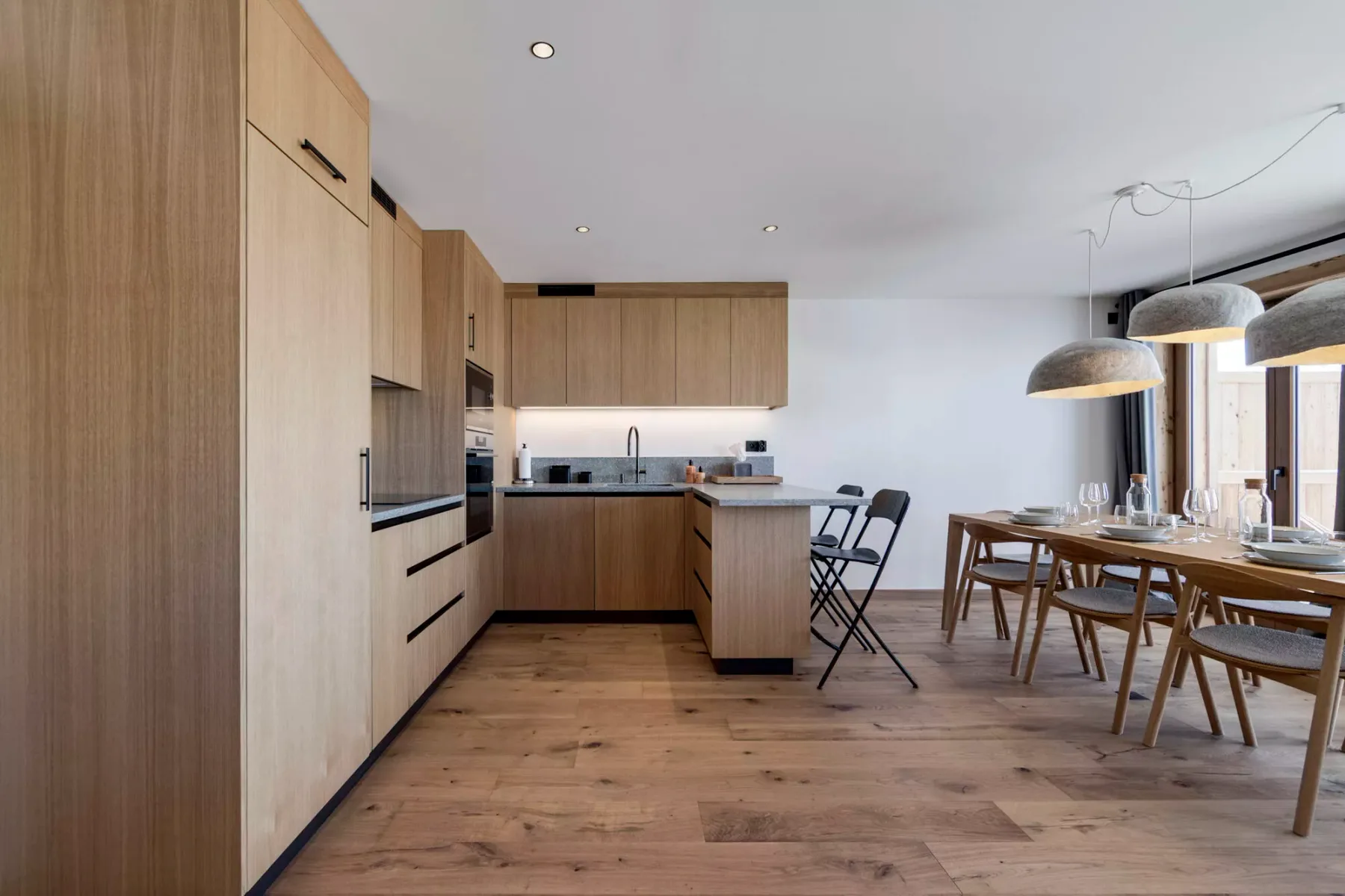 Una cocina moderna se abre a un comedor con una mesa de madera y sillas.