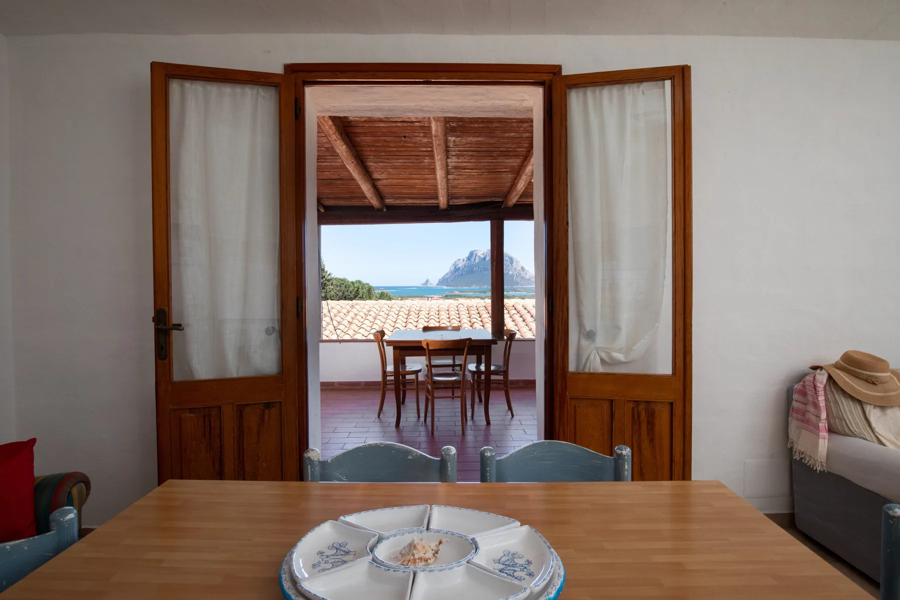 Una mesa de comedor da a unas puertas de madera abiertas y una terraza con asientos.