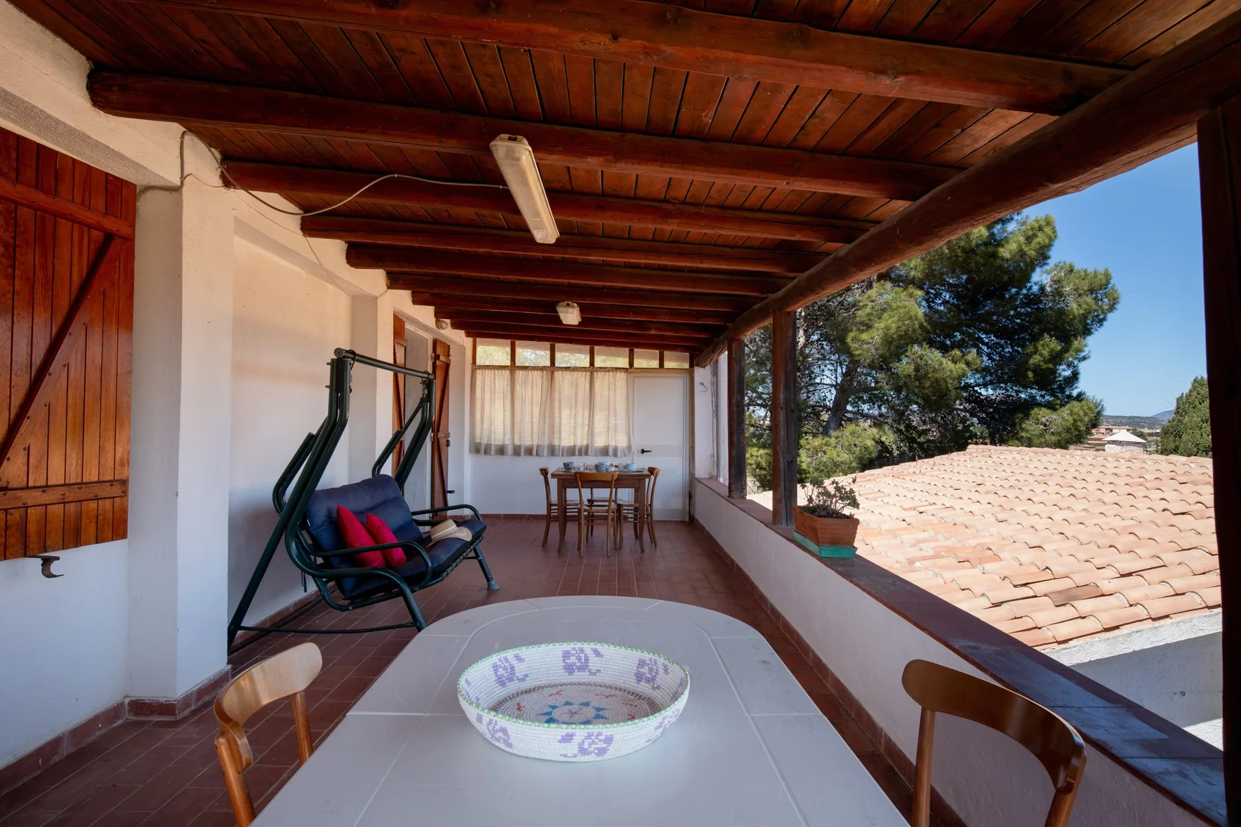 Una terraza cubierta con mesa y asientos da a tejados de tejas y árboles.