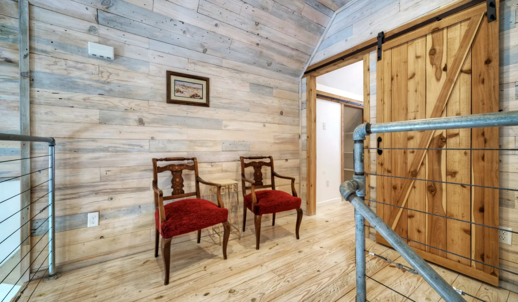 Un descansillo revestido de madera tiene dos sillas con cojines rojos junto a una gran puerta corrediza de madera.