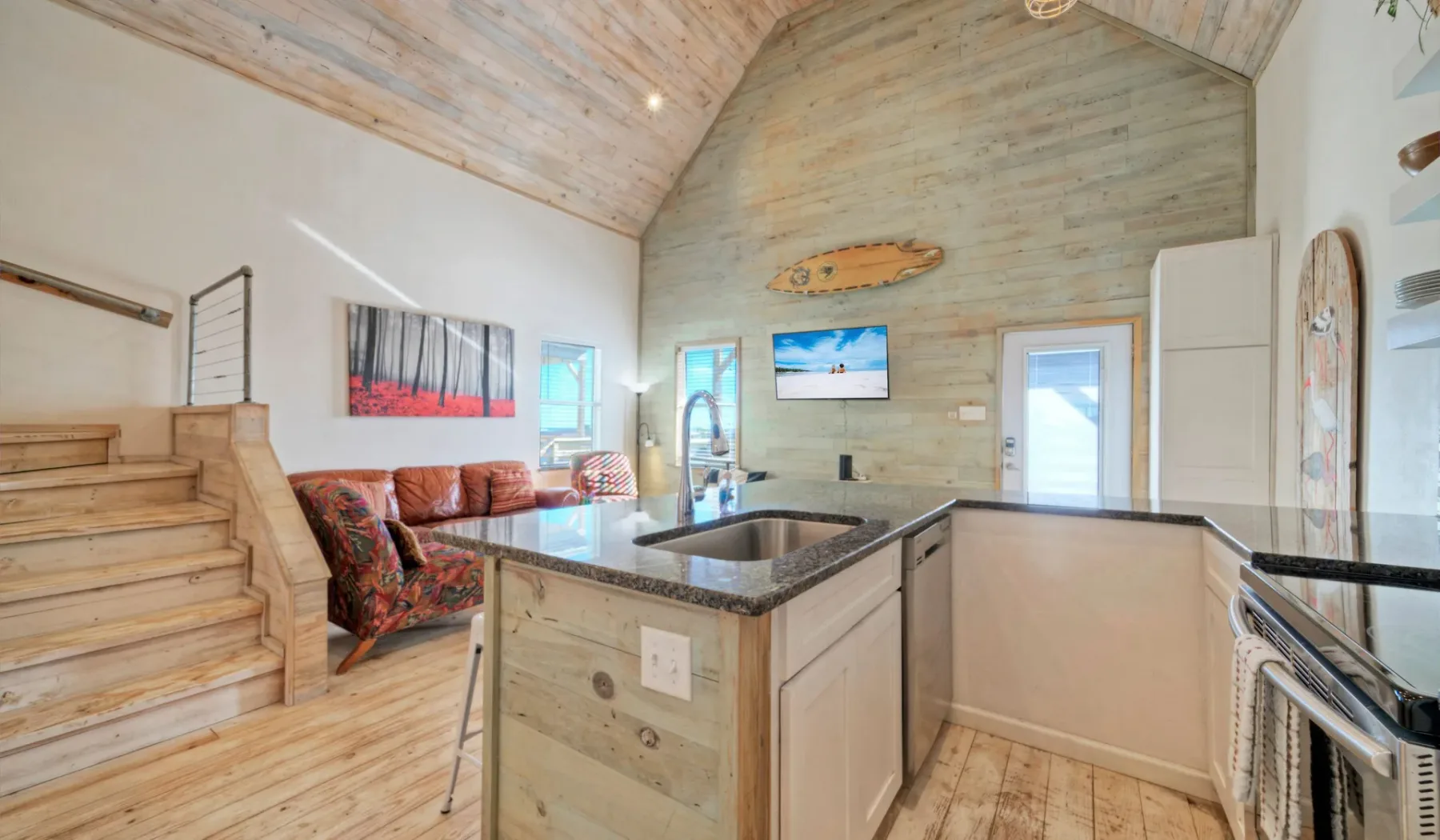 Una sala con techo abovedado, isla de cocina, asientos y un televisor.
