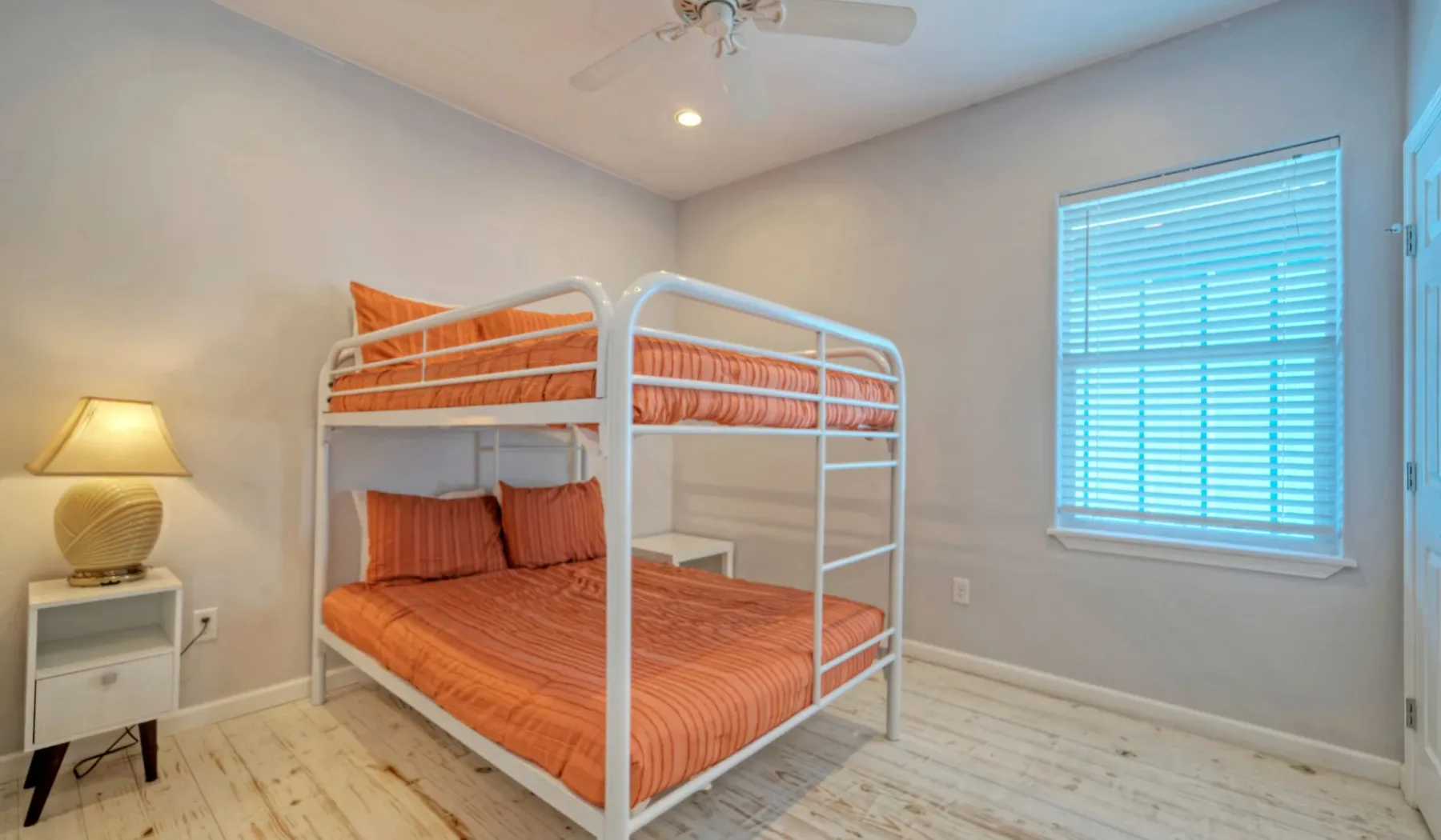 Un dormitorio con una litera blanca y ropa de cama naranja.