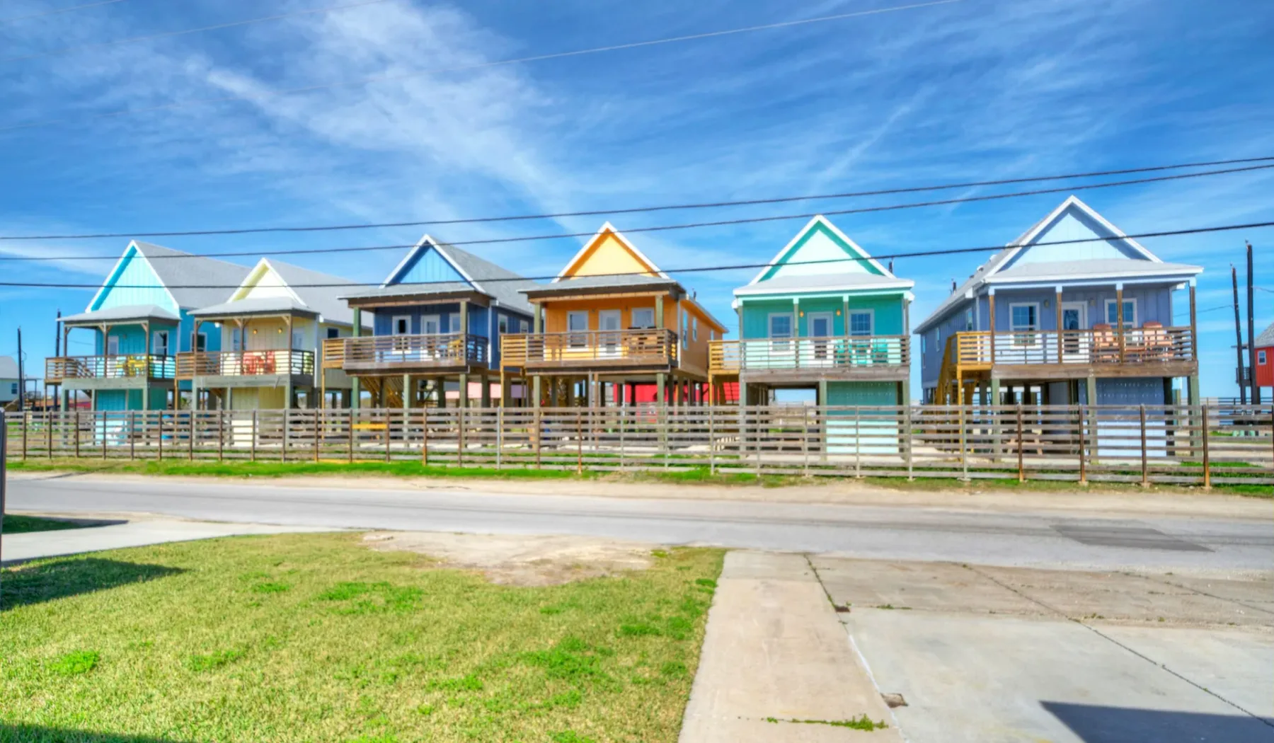 Una hilera de coloridas casas elevadas junto a la playa está junto a una carretera bajo un cielo azul.