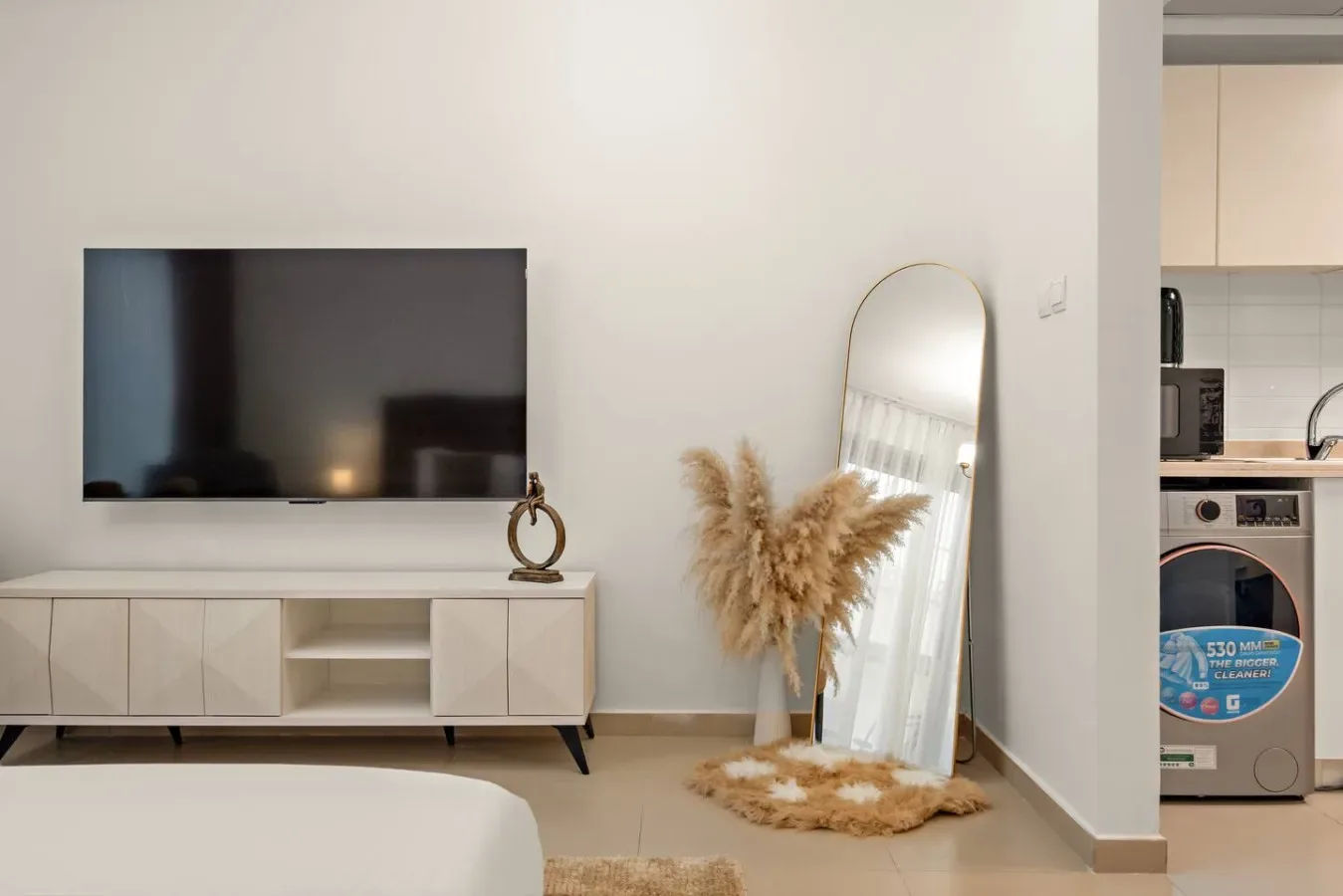 Una sala de estar con televisor en la pared, mueble bajo y espejo alto.