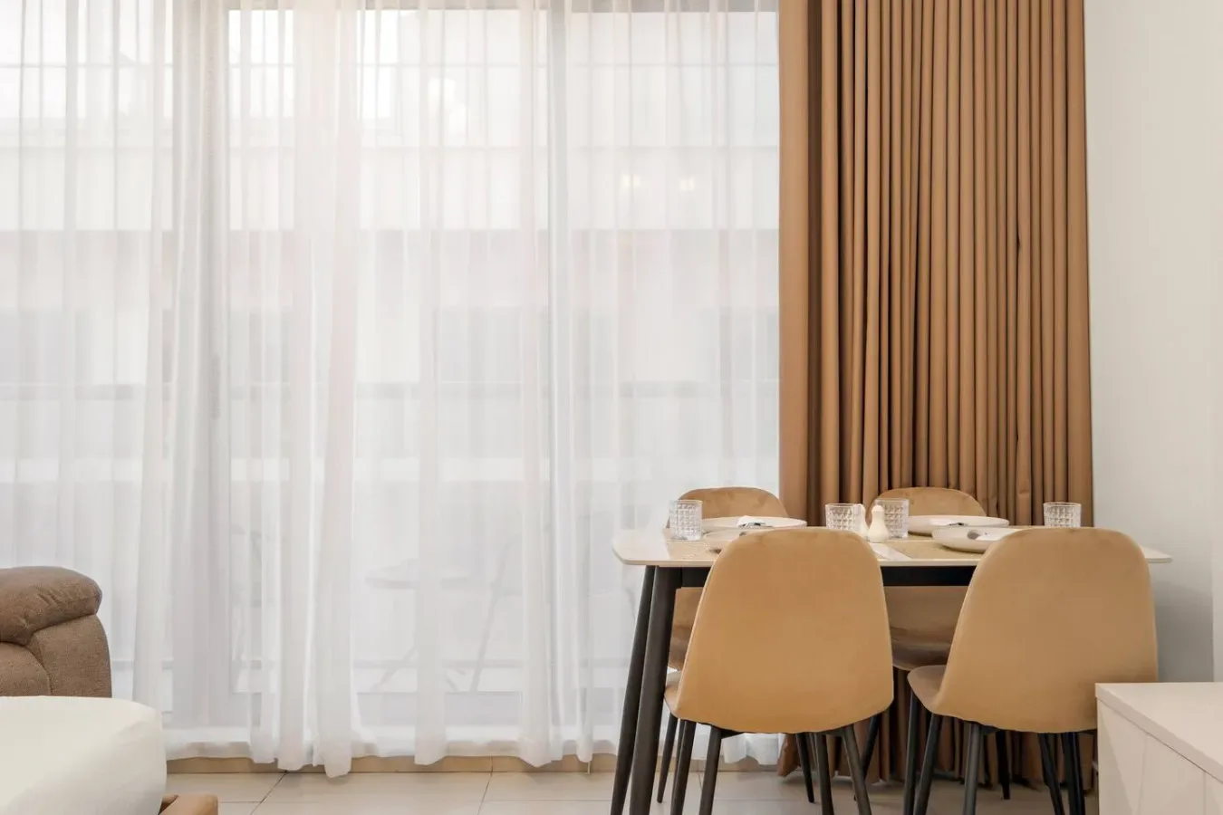 Comedor con mesa y sillas junto a ventanas altas con cortinas translúcidas.