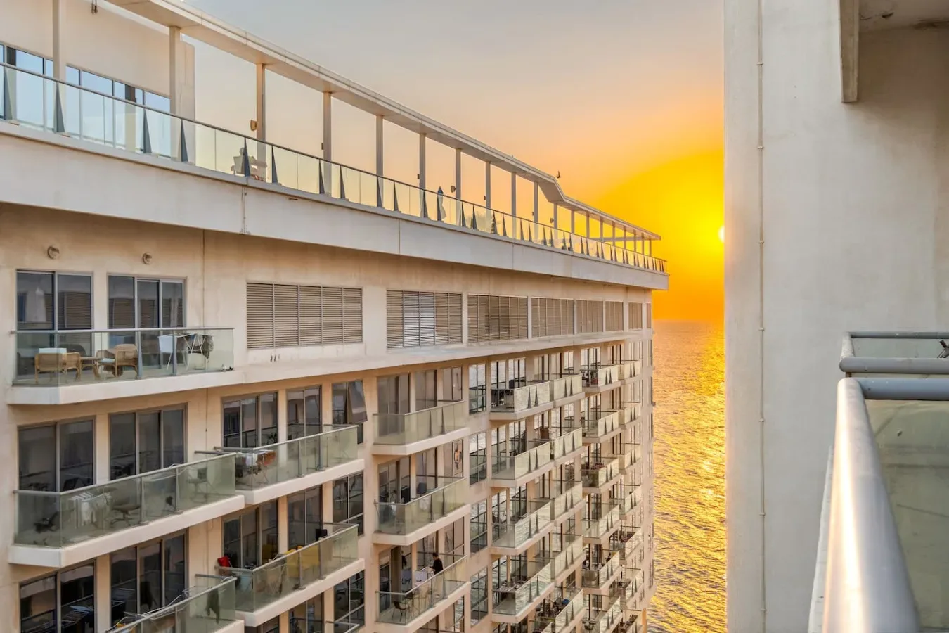 Un edificio de apartamentos frente al mar, con balcones, mira al océano al atardecer.