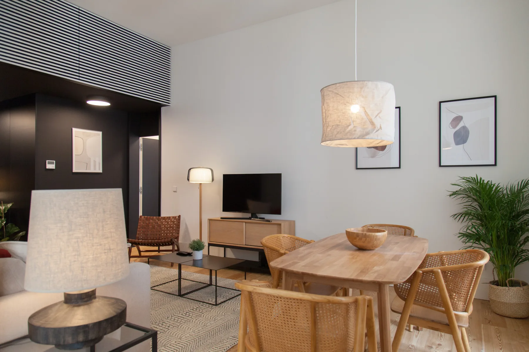 Una luminosa sala de estar y comedor con televisor, mesa de madera y asientos de fibras tejidas.
