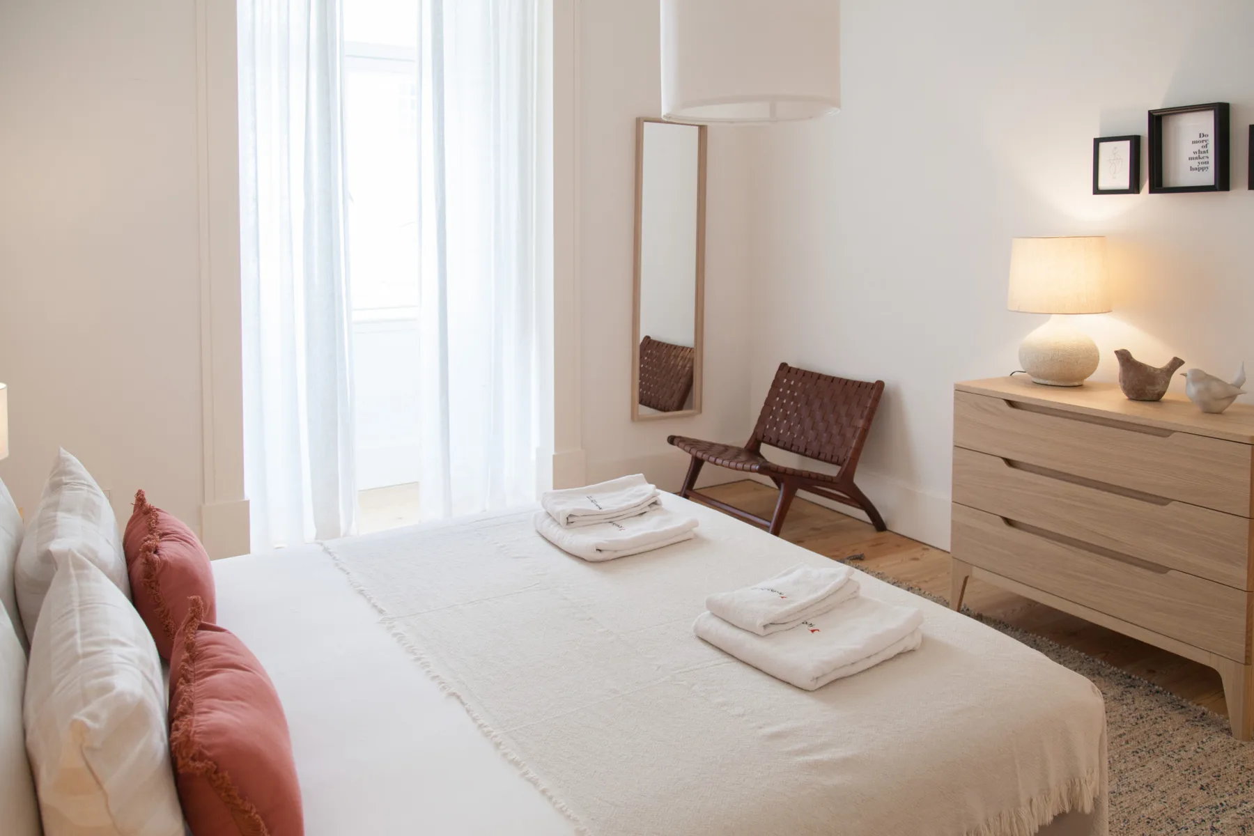 Un dormitorio luminoso con una cama bien hecha y asientos junto a la ventana.