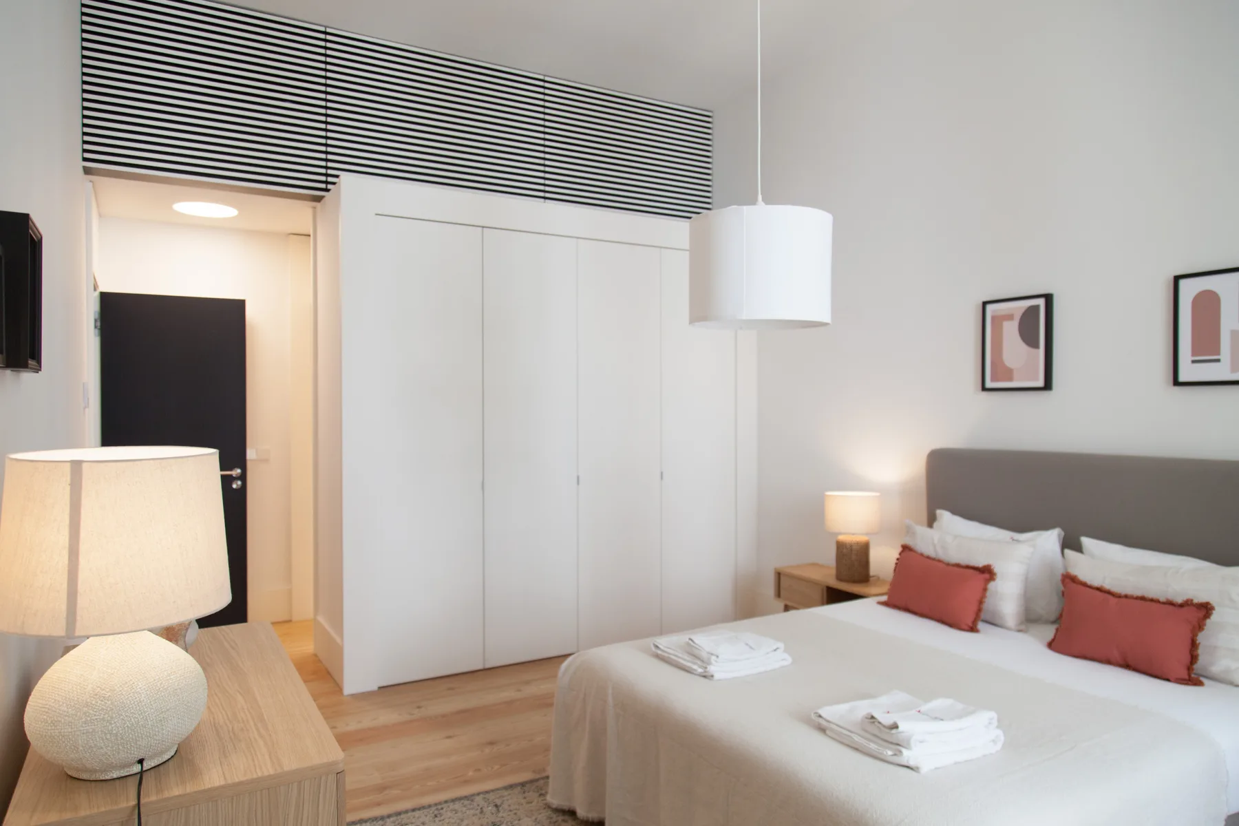 Un dormitorio luminoso con una cama tendida, mesillas y armarios empotrados.