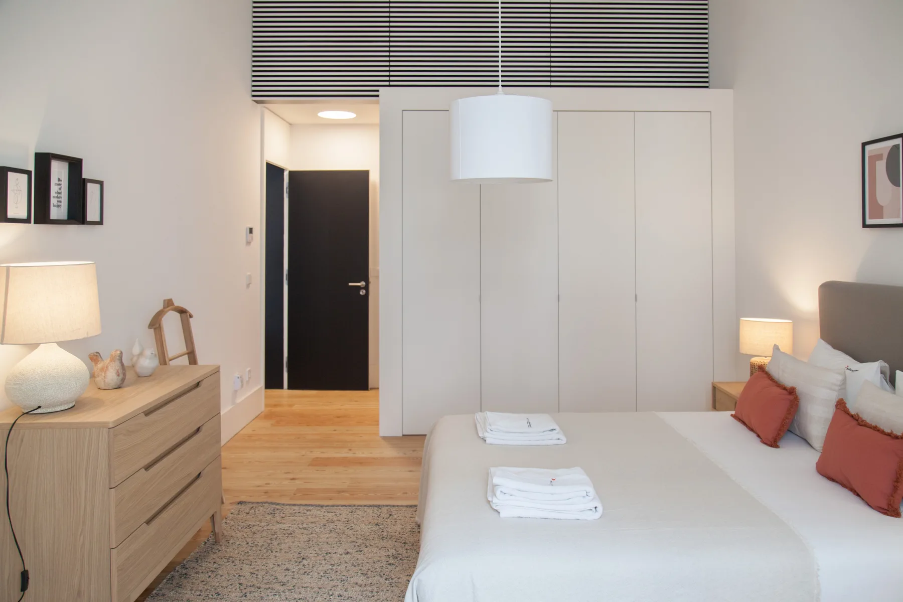 Un dormitorio luminoso con una cama, toallas dobladas y una cómoda de madera.