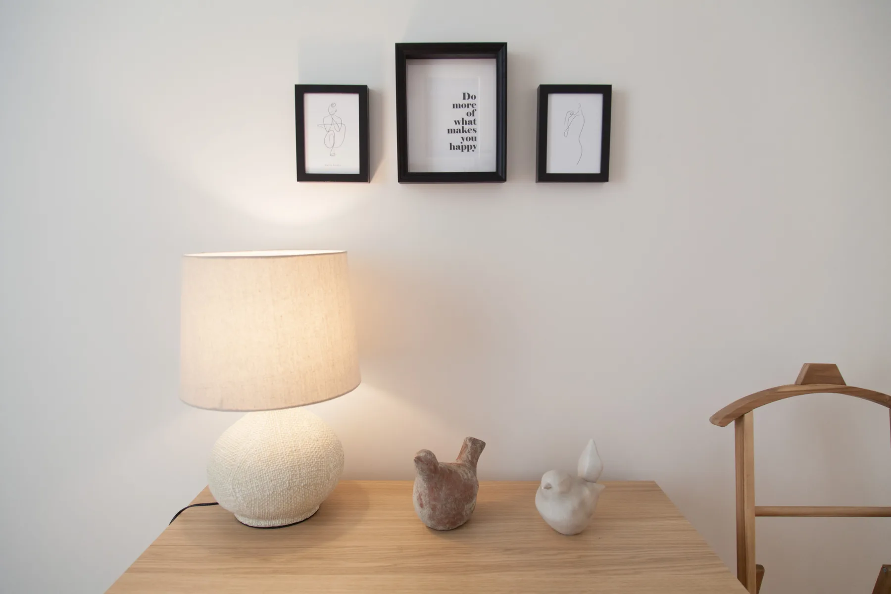Una mesita de dormitorio tiene una lámpara encendida y dos pequeñas figuras decorativas.