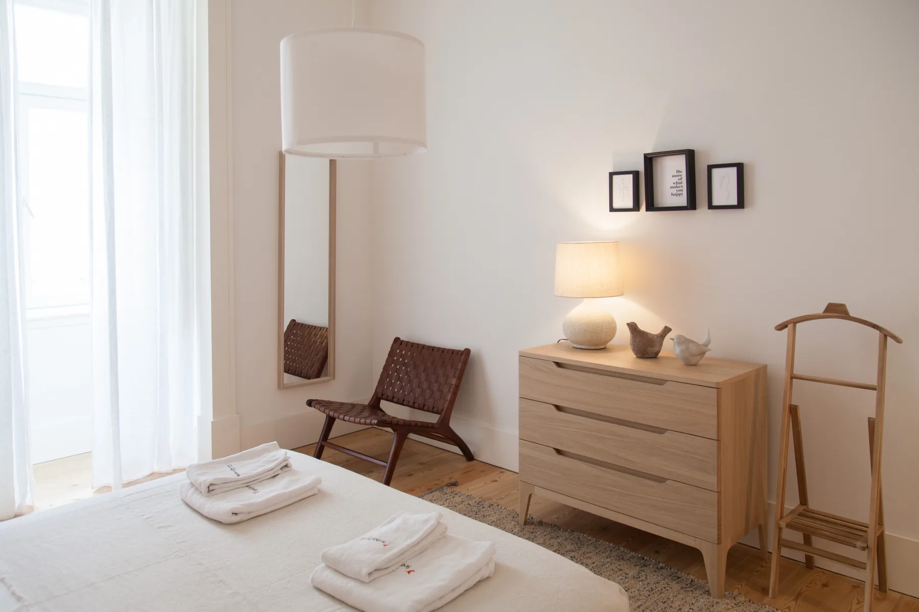 Un dormitorio luminoso con una cama, una cómoda de madera y asientos junto a una ventana grande.