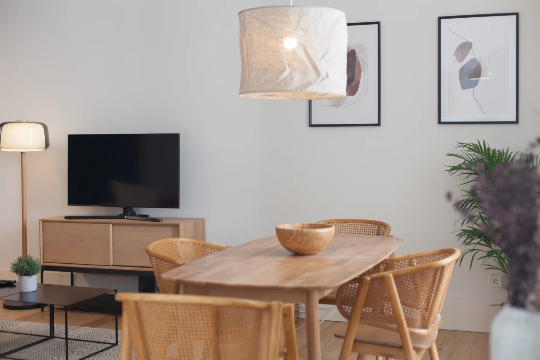 Comedor con mesa de madera y asientos tejidos junto a un televisor.