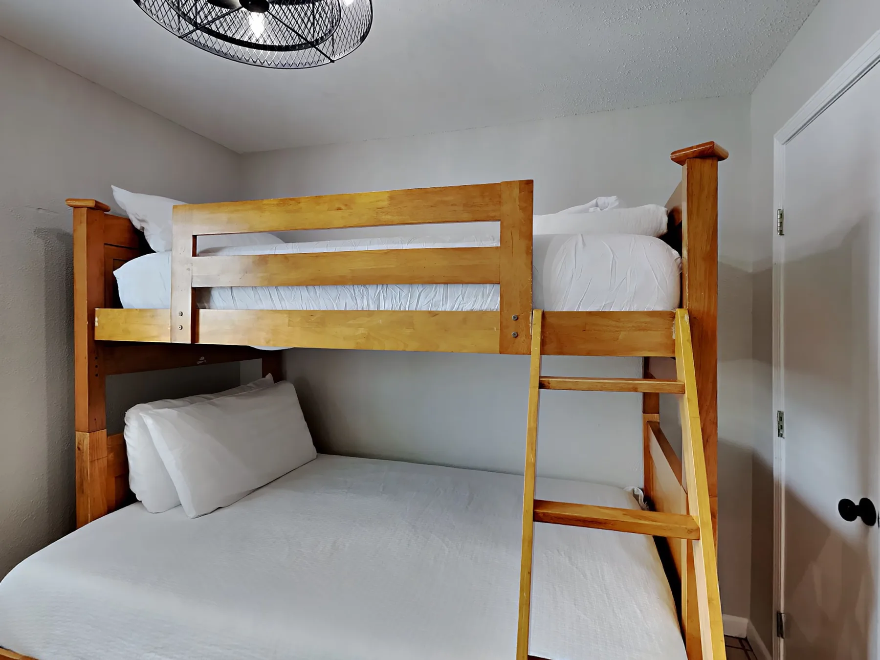 Una litera con ropa de cama blanca y una escalera de madera ocupa el dormitorio.