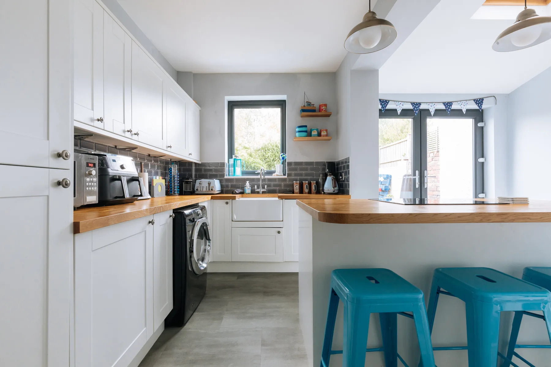 A bright kitchen with white cabinets, a wood counter, and teal stools.