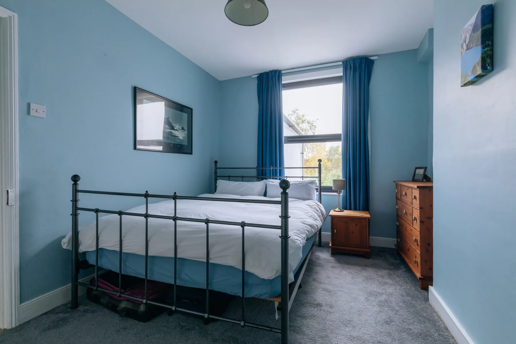 A bedroom with a metal bed, blue walls, and a large window.