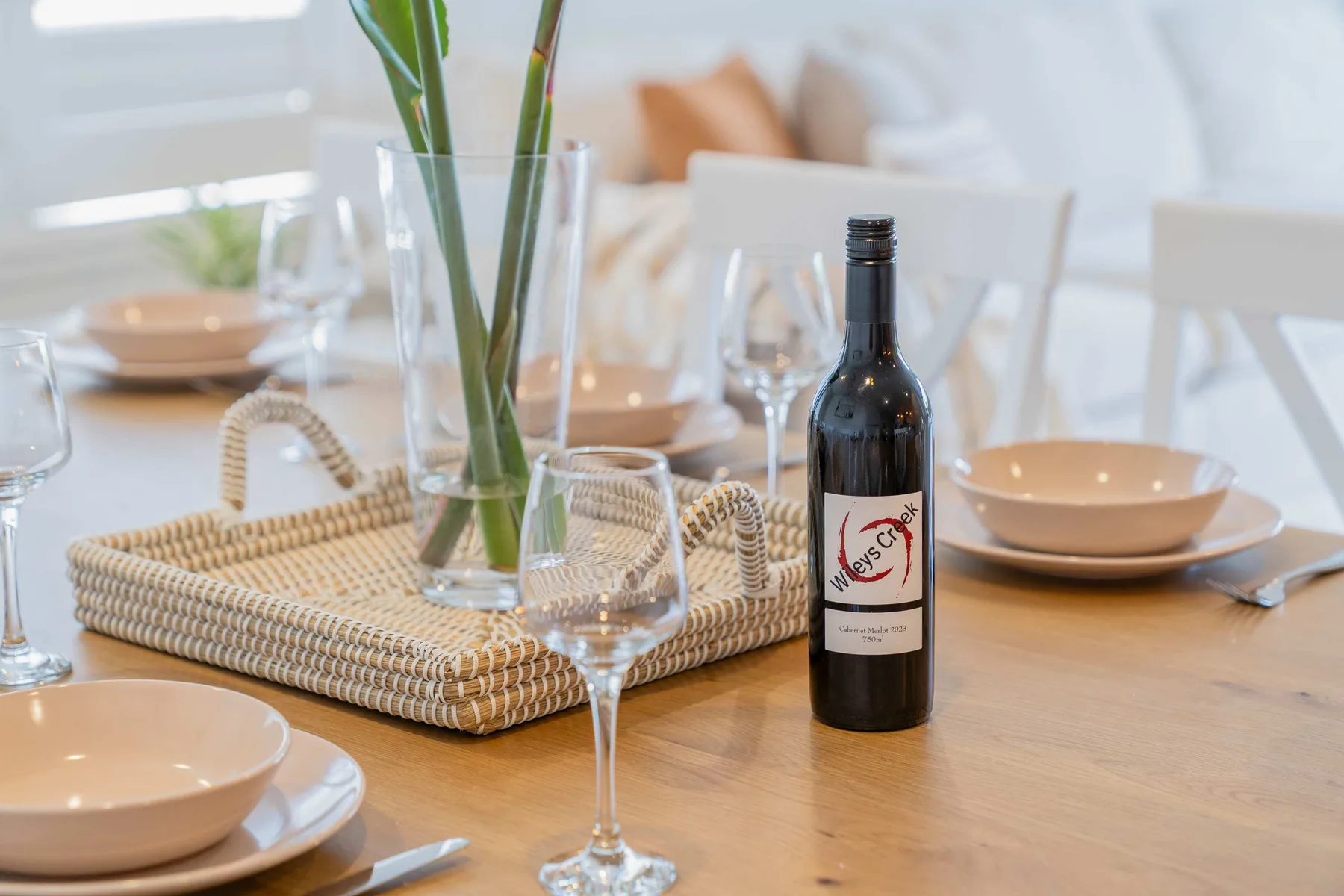 Una mesa de comedor está puesta con platos, copas y una botella de vino.