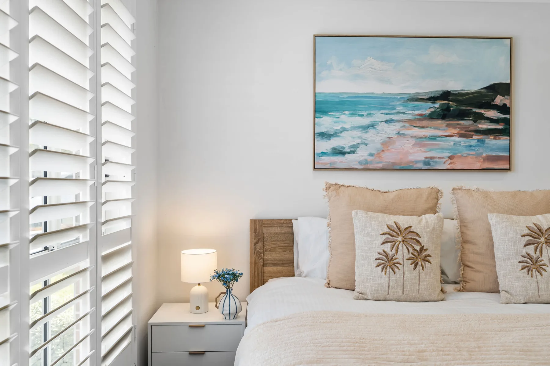 Un dormitorio con una cama, una mesita de noche y una imagen costera.
