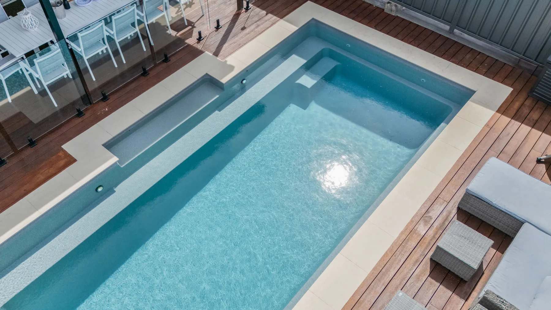 Una piscina está rodeada de una tarima de madera y asientos de descanso.