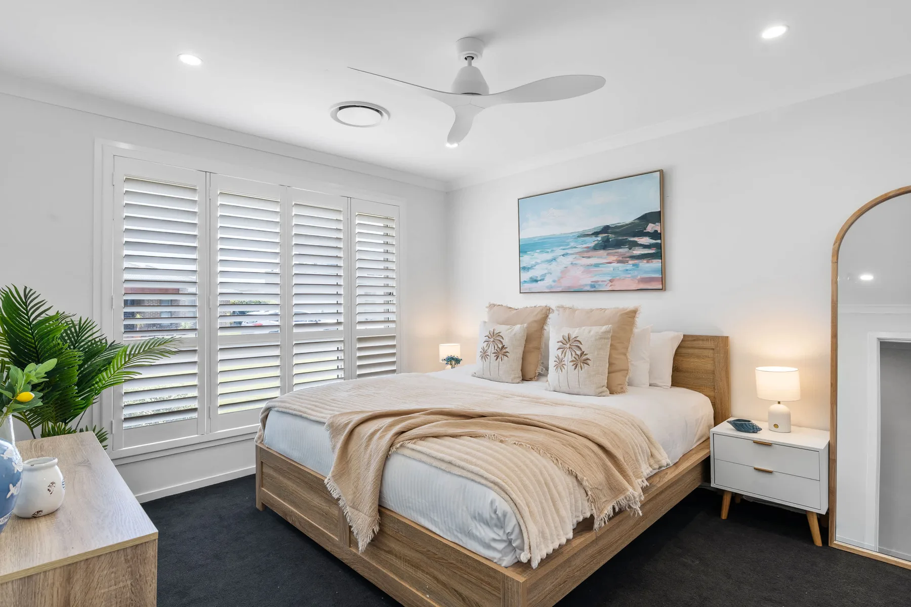 Un dormitorio luminoso con una cama de madera, ropa de cama en capas y amplias ventanas con persianas.