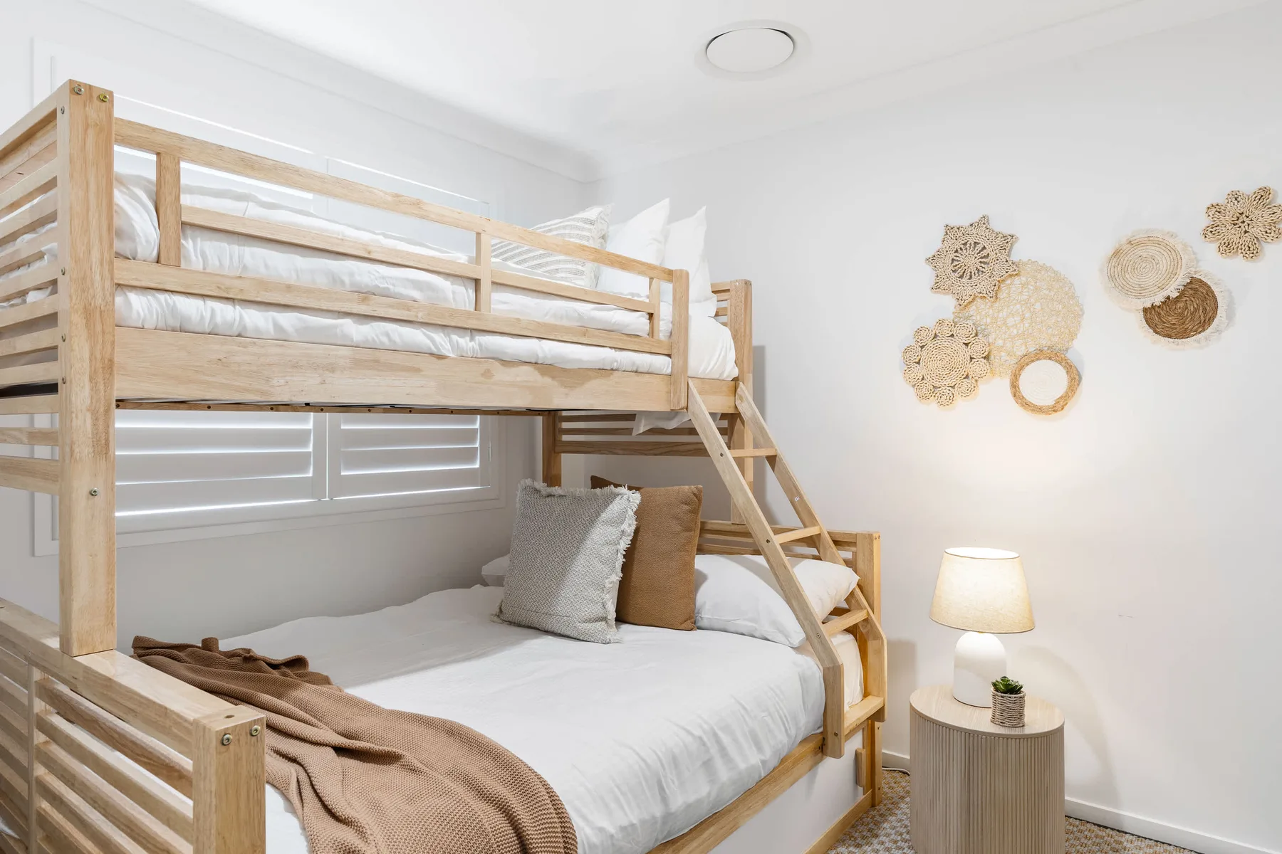 Un dormitorio con una litera de madera, ropa de cama blanca y adornos tejidos en la pared.