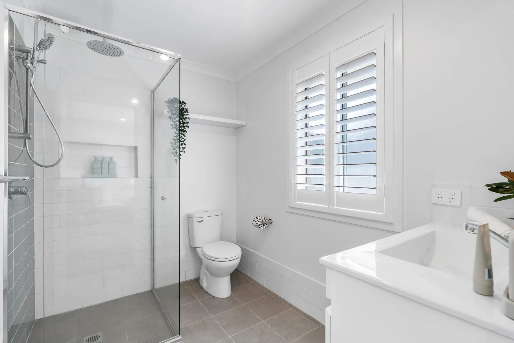 Un baño luminoso con ducha de vidrio, inodoro y lavabo blanco.